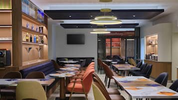 A modern restaurant interior with round tables, cushioned booths, and a bar area.