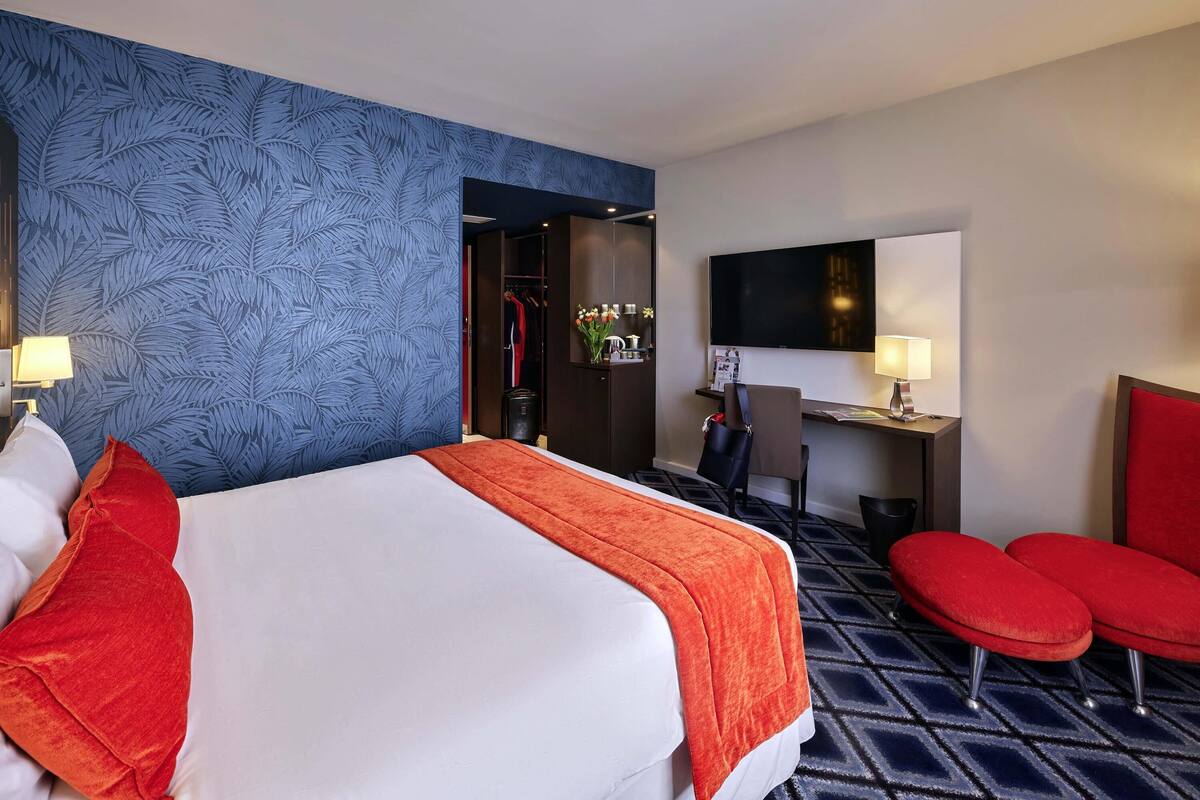 A hotel room with a bed, a desk, a TV, and a seating area.