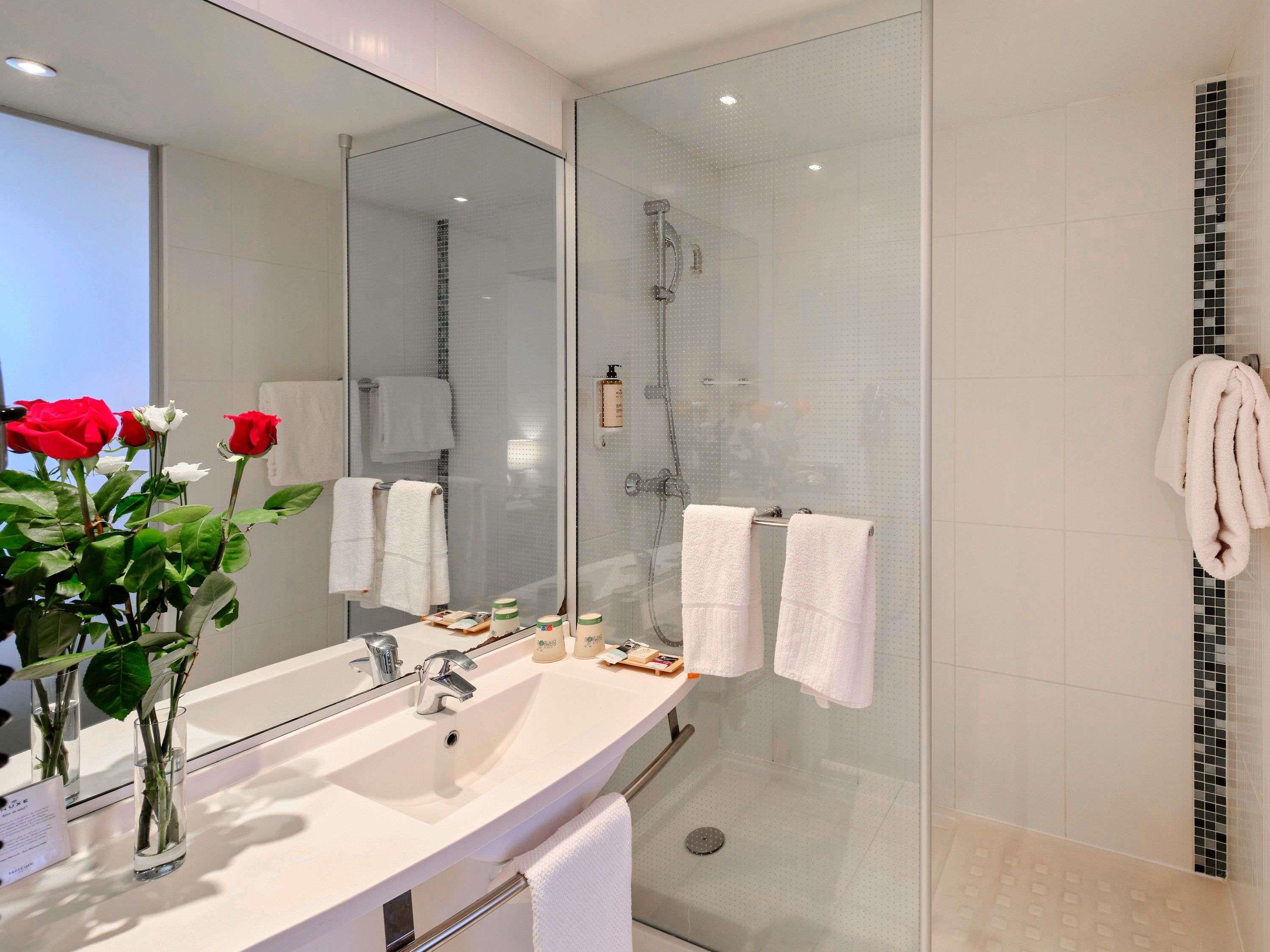 A modern bathroom with a glass shower enclosure, a large mirror, and a vanity with a sink and toiletries.