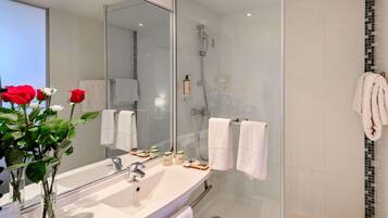 Un baño moderno con cabina de ducha de vidrio, un espejo grande y tocador con lavamanos y artículos de aseo.