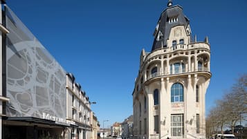 A street view with a prominent building featuring a tower with a spire and arched windows.