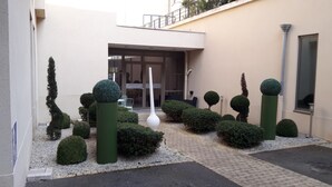 A courtyard with neatly trimmed hedges, a tall white sculpture, and a building entrance. - Mercure Chartres Centre Cathédrale (Chartres)