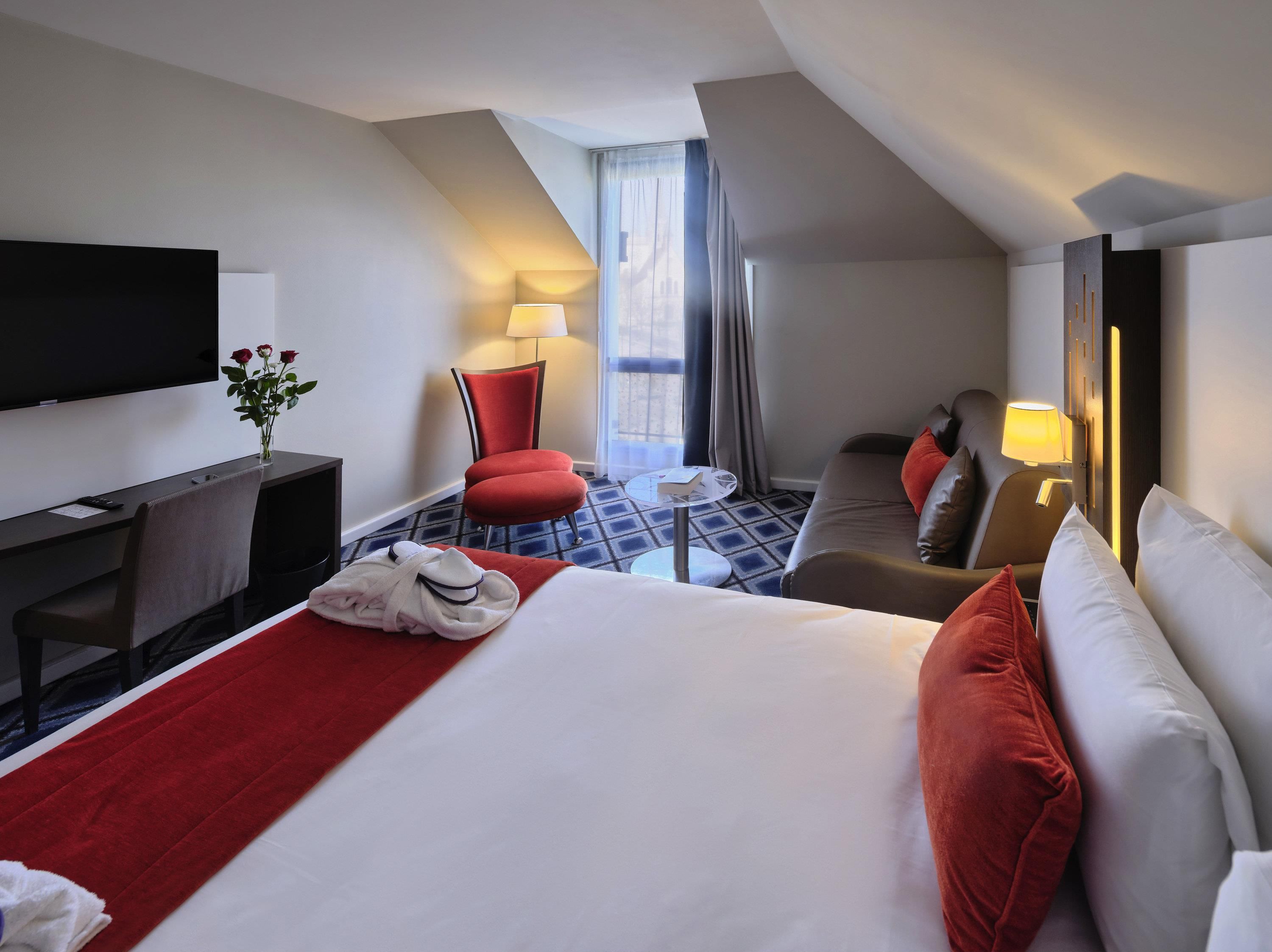 A hotel room with a bed, a desk, a TV, a chair, a sofa, and a window with curtains.