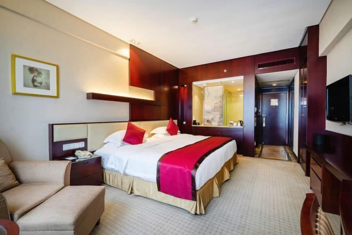Ein Hotelzimmer mit Bett, Stuhl, Nachttisch, Spiegel und Fernseher.
