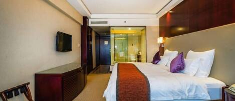 A hotel room with a bed, a TV mounted on the wall, a desk, and a mirror.