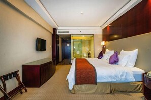 Habitación de hotel con cama, televisión montada en la pared, escritorio y espejo.