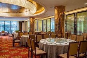 A dining area with round tables, chairs, and a chandelier.