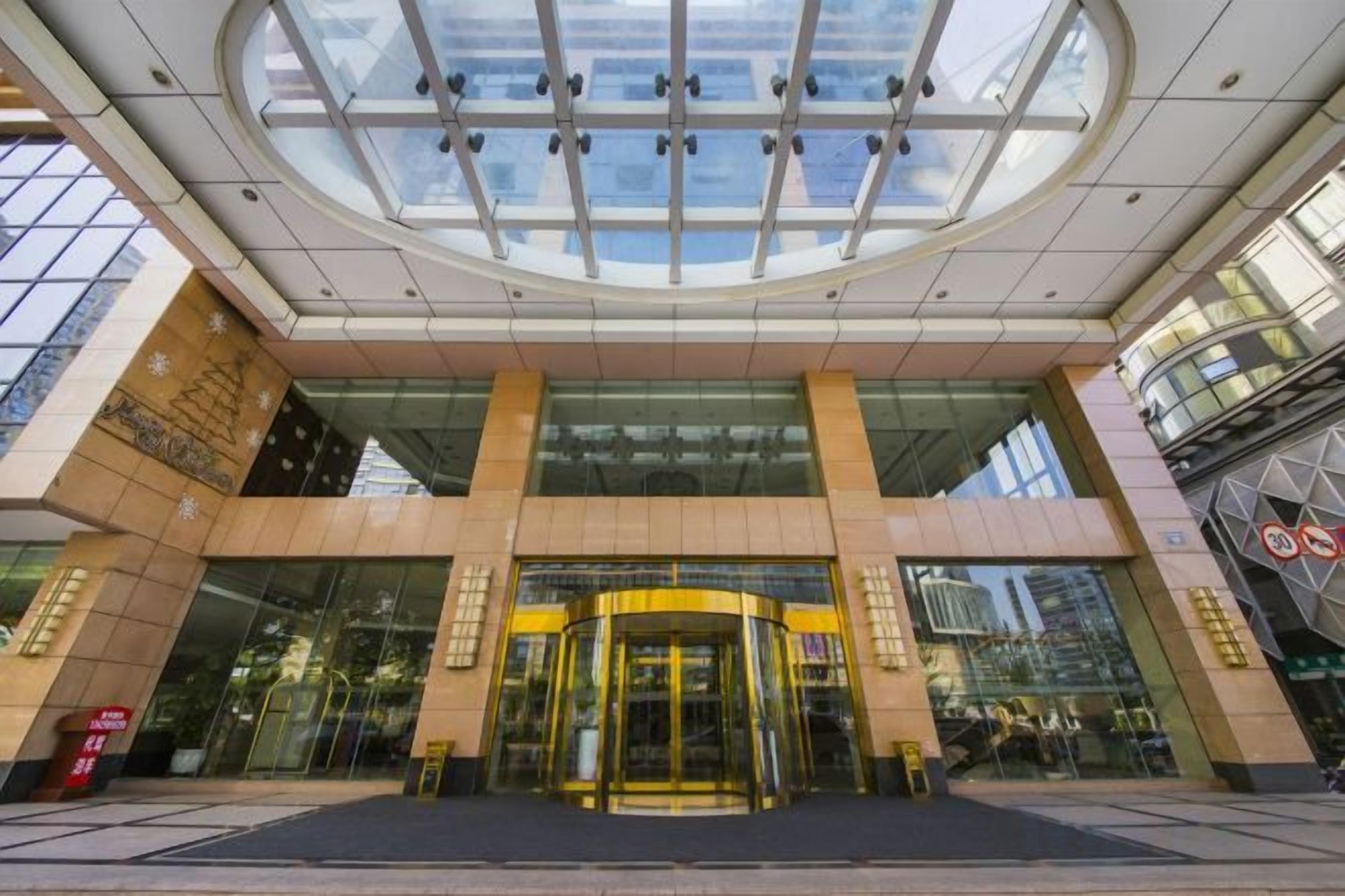 A hotel entrance with a glass facade, a revolving door, and a large glass ceiling.