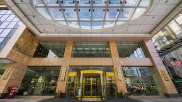 A hotel entrance with a glass facade, a revolving door, and a large glass ceiling.