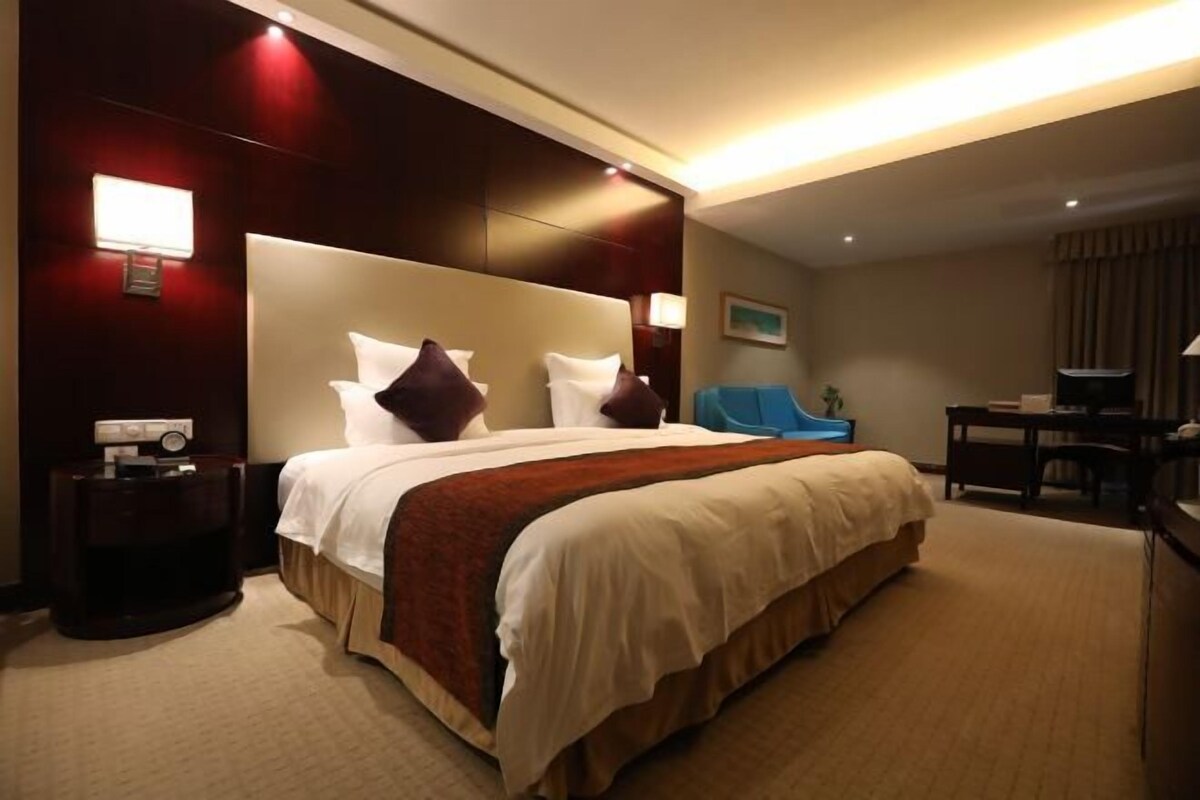 A hotel room with a large bed, a bedside table, a desk, and a chair.
