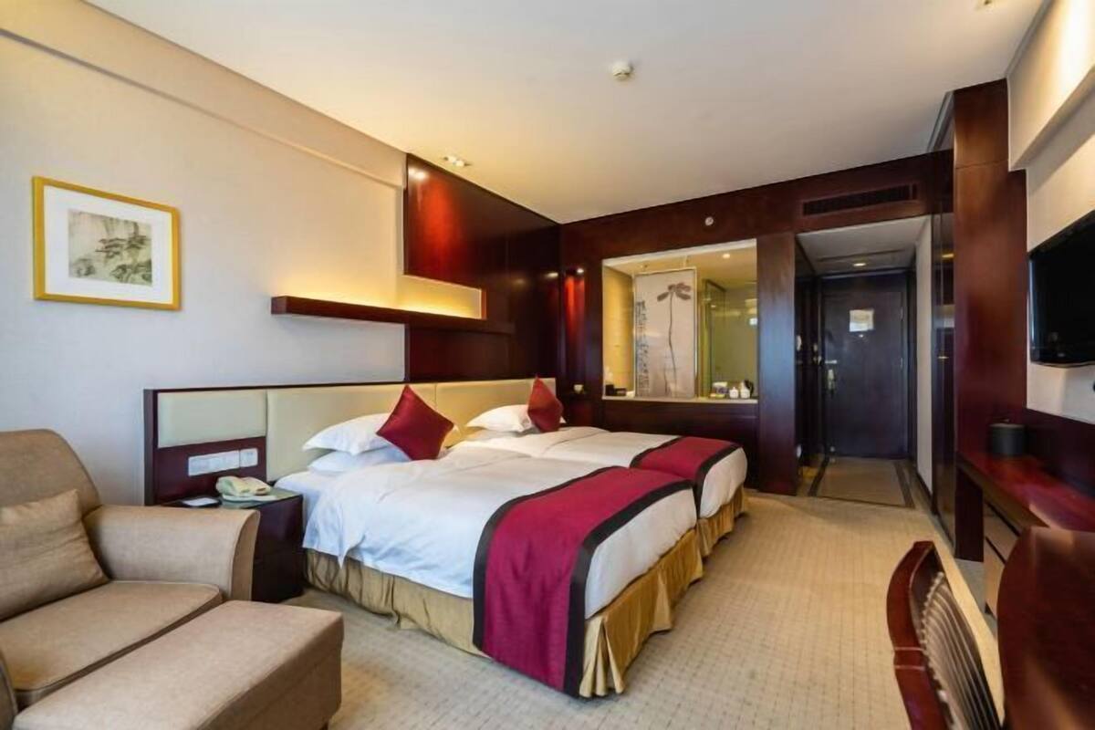 Ein Hotelzimmer mit zwei Betten, einem Sofa, einem Fernseher und einem Spiegel.