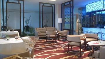 A hotel lobby with a dining area, sofas, a bar, and a large window.