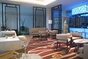 A hotel lobby with a dining area, sofas, a bar, and a large window.
