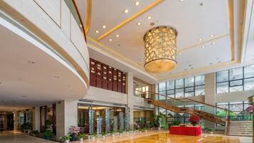 A spacious lobby with a high ceiling, a central chandelier, and a staircase leading to an upper level.