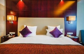 A hotel room with a large bed, two bedside lamps, a nightstand, and a wooden headboard. - Fubang International Hotel (Hangzhou)