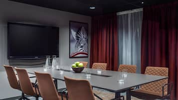 A conference room with a large table, six chairs, a flat-screen TV, a framed artwork, and red curtains.