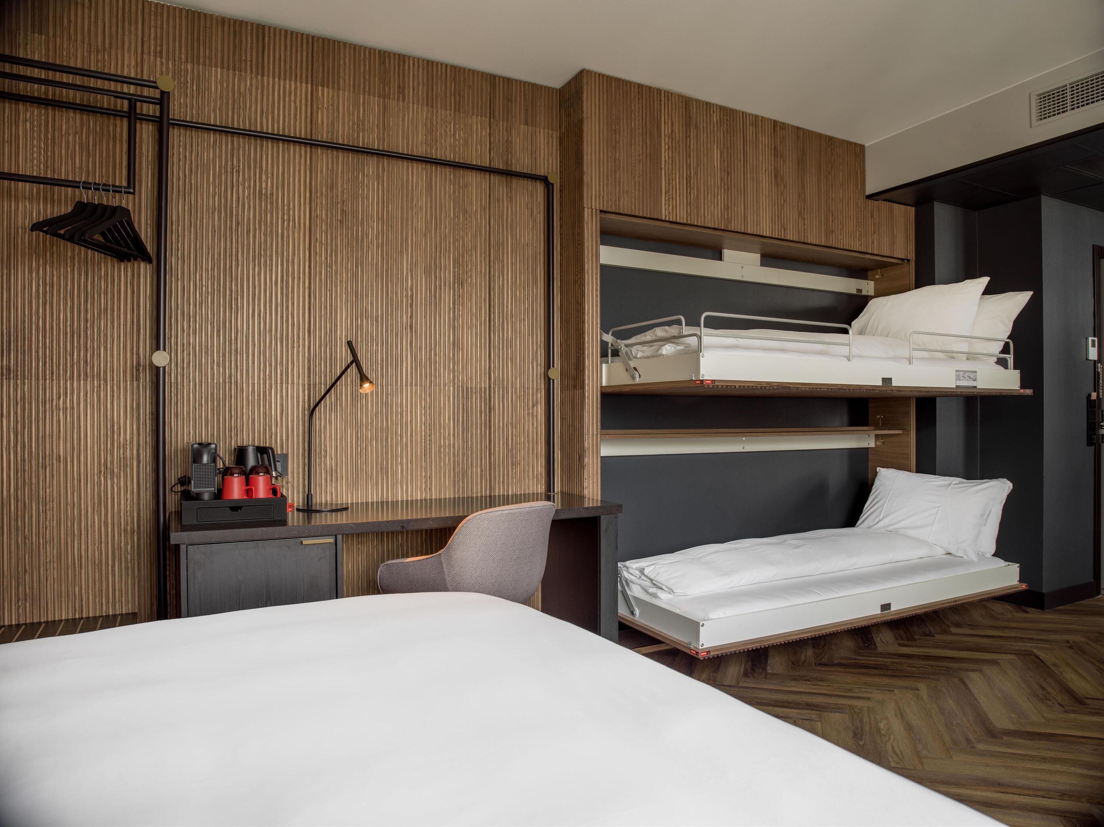 Quarto de hotel com beliche, uma escrivaninha com luminária e uma cadeira.