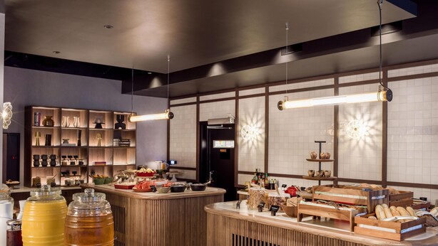 A modern bar area with wooden shelves, a central counter with food and drink items, and pendant lighting. - Radisson RED Oslo City Centre, A Verified Net Zero Hotel (Oslo)