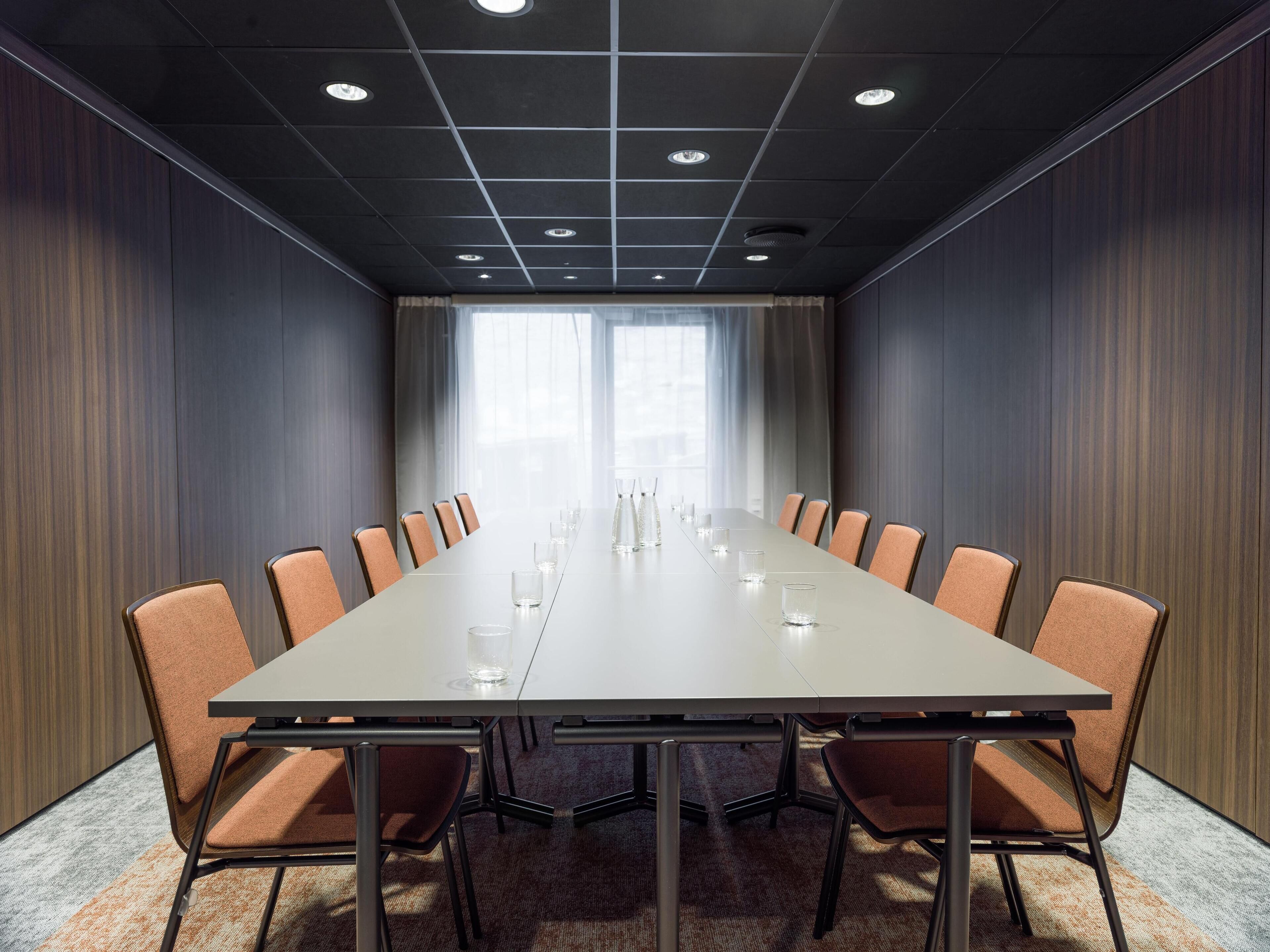 A conference room with a long table, chairs, and a carpeted floor.