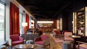 A modern lounge area with red upholstered chairs, a bar in the background, and a mix of seating options including sofas and ottomans. - Radisson RED Oslo City Centre, A Verified Net Zero Hotel (Oslo)