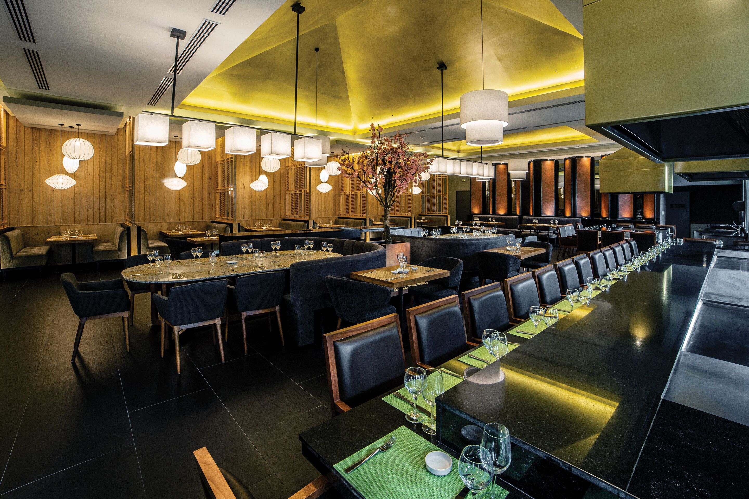 Un restaurant moderne doté de nombreuses tables et chaises, d’un long comptoir et d’un éclairage suspendu.