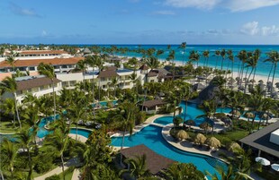 A resort with multiple swimming pools, palm trees, and a view of the ocean.
