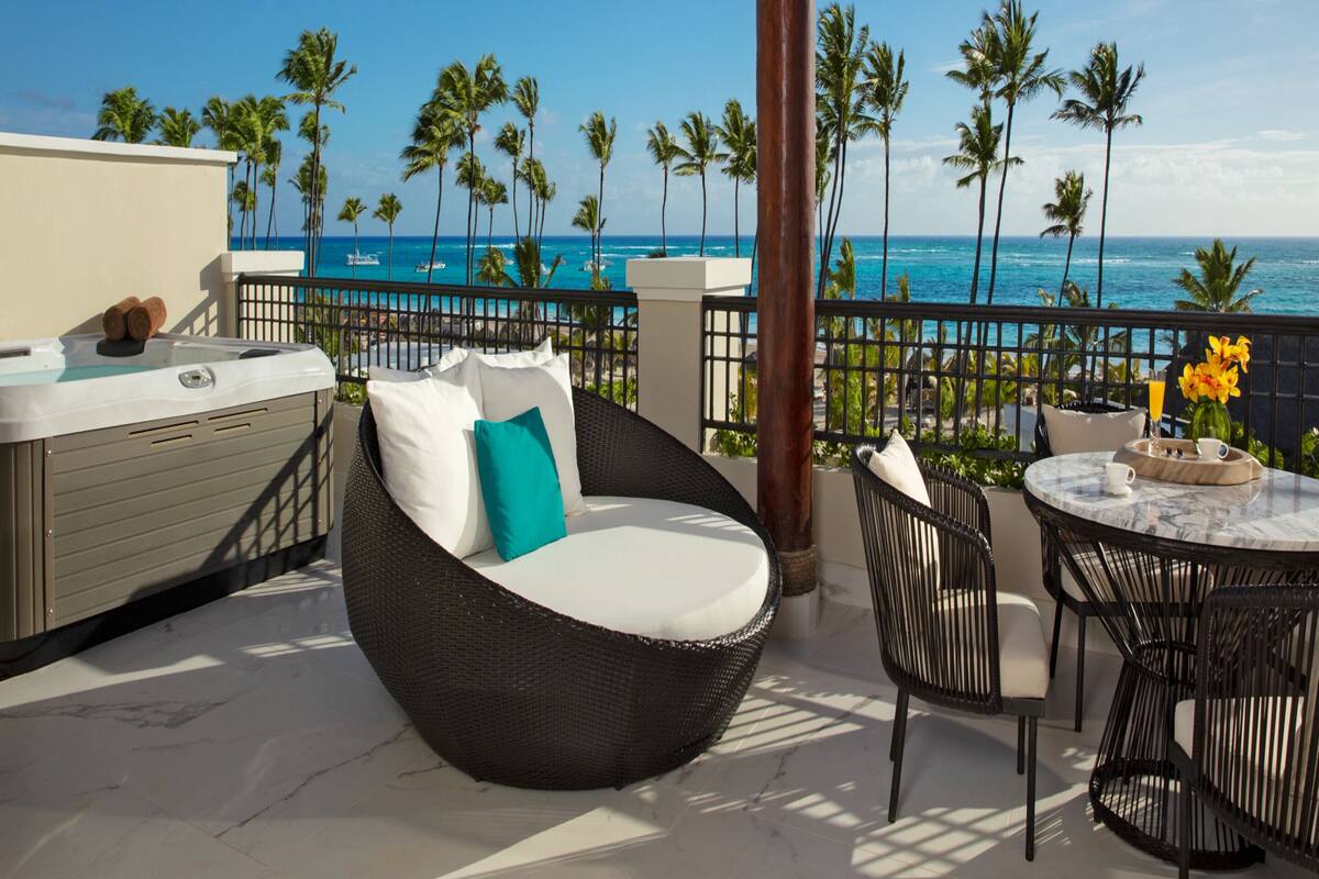 A balcony with a hot tub, wicker furniture, and a table with a vase of flowers.