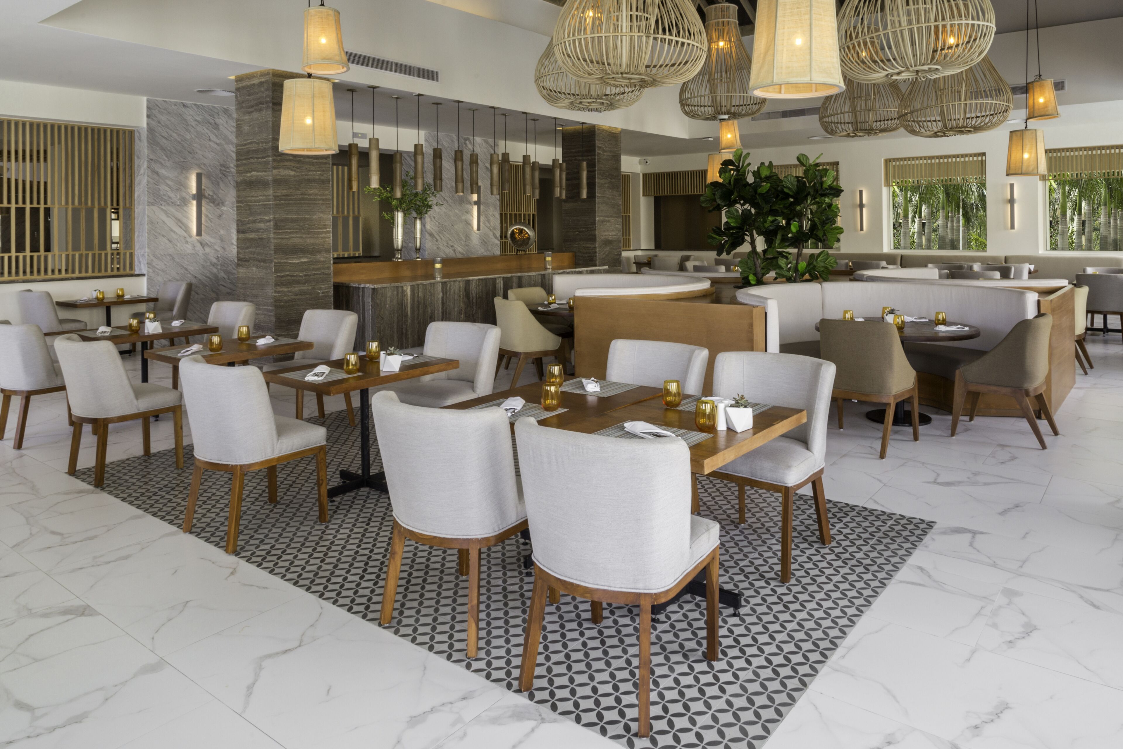 Een modern restaurant met hoge tafels en stoelen, hangende rieten kroonluchters en een marmeren vloer.