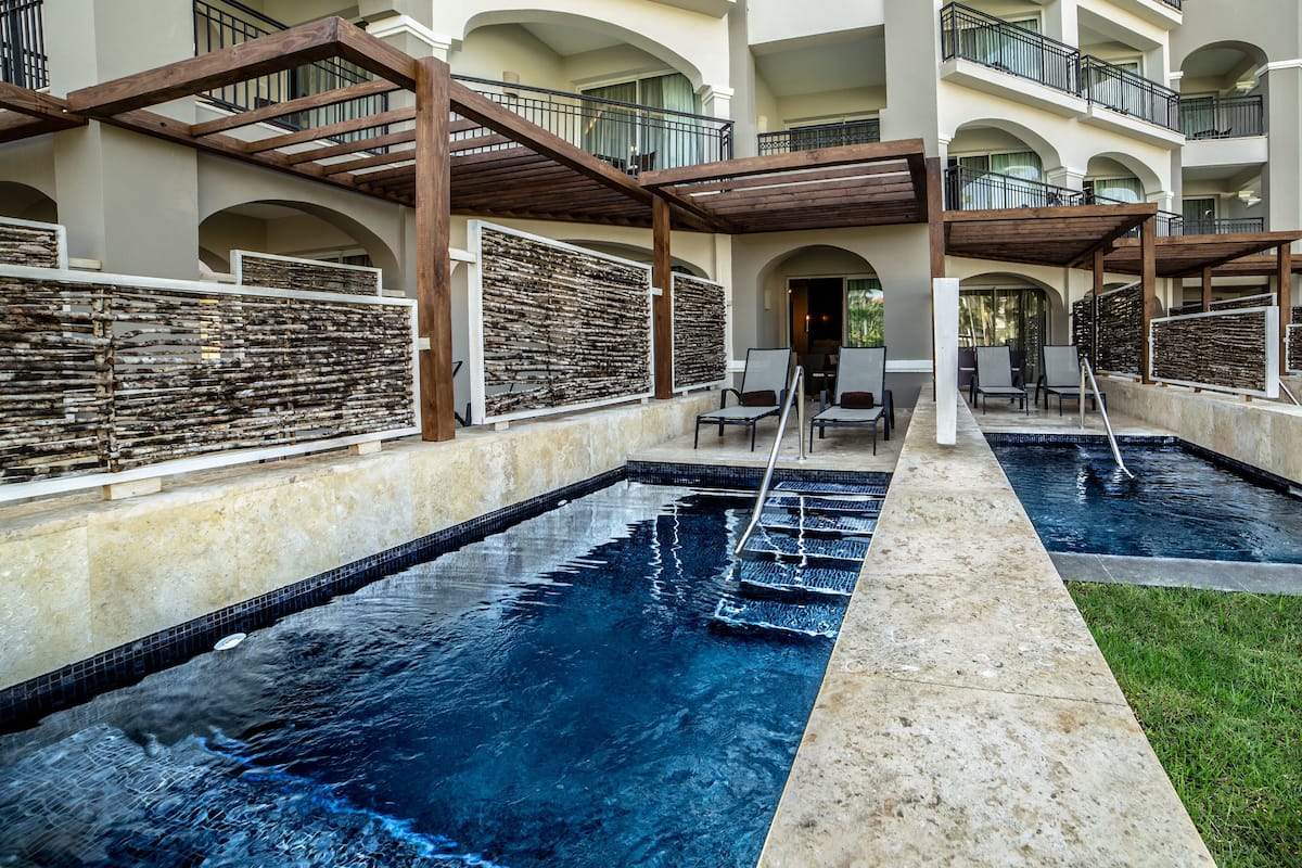 A pool area with two separate pools, wooden pergolas, and lounge chairs.