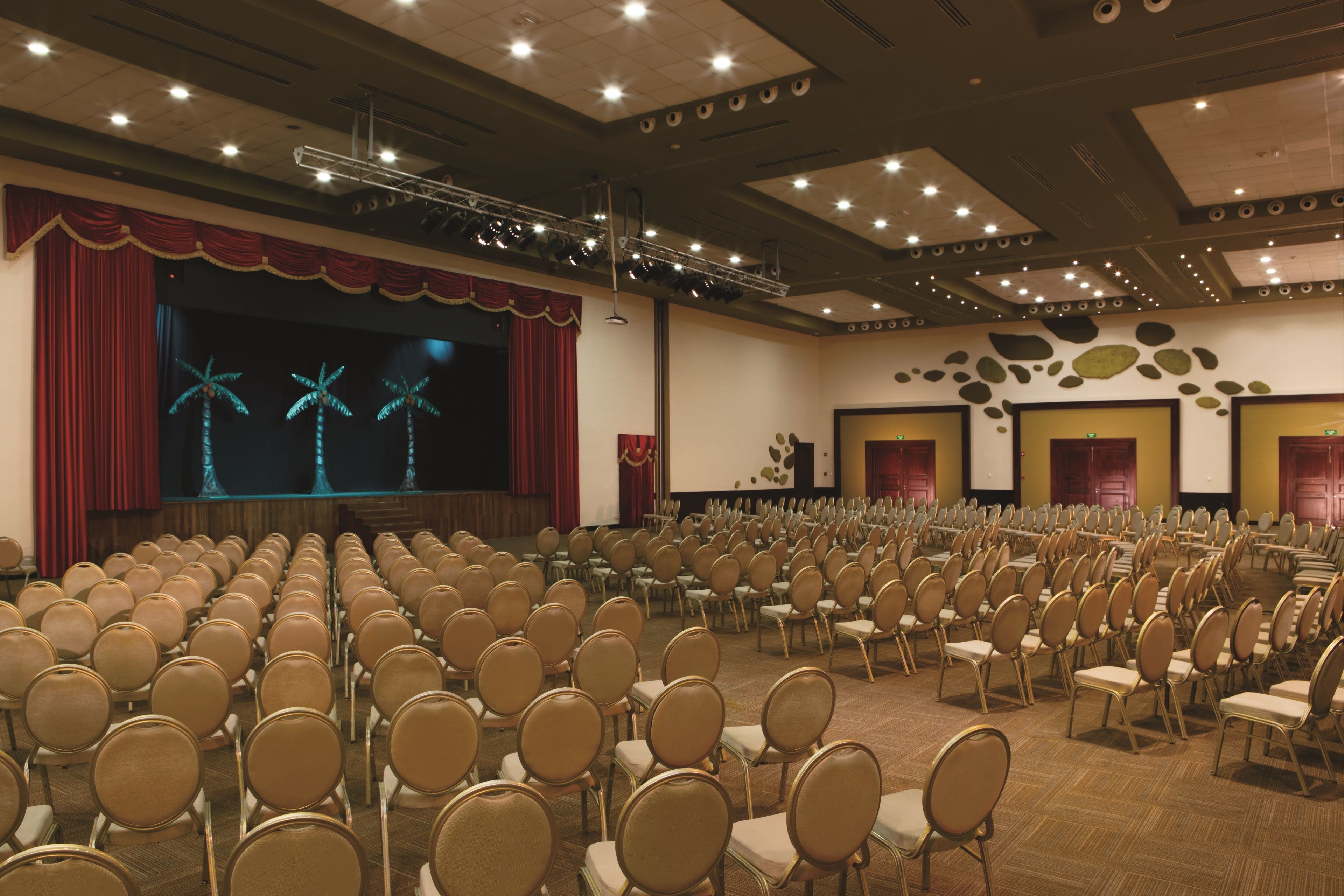 Une salle de conférence avec des rangées de chaises, une scène avec des rideaux et un grand écran.