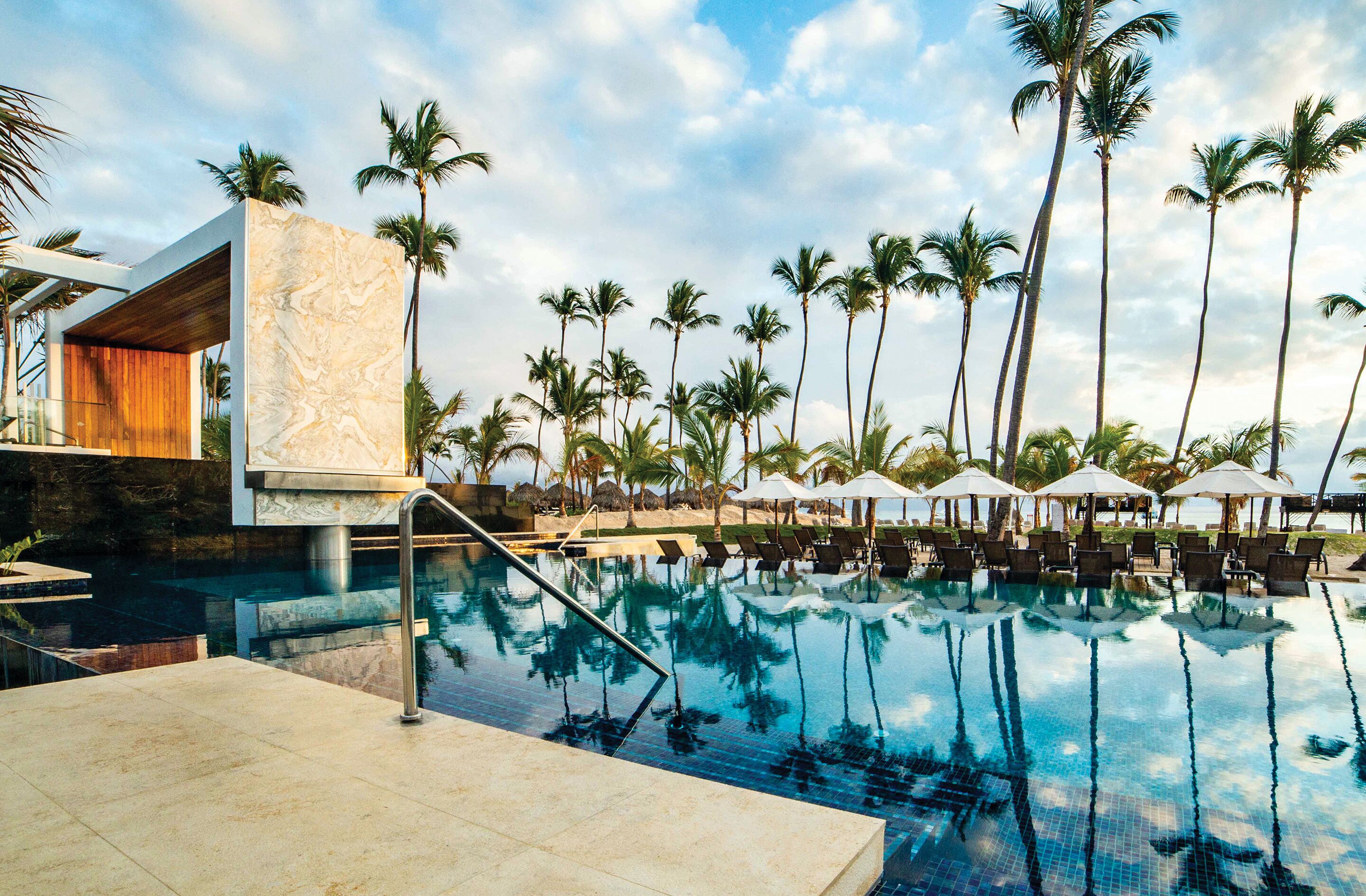 A swimming pool with lounge chairs and umbrellas, surrounded by palm trees.