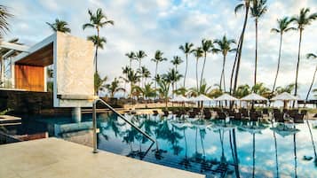 A swimming pool with lounge chairs and umbrellas, surrounded by palm trees.