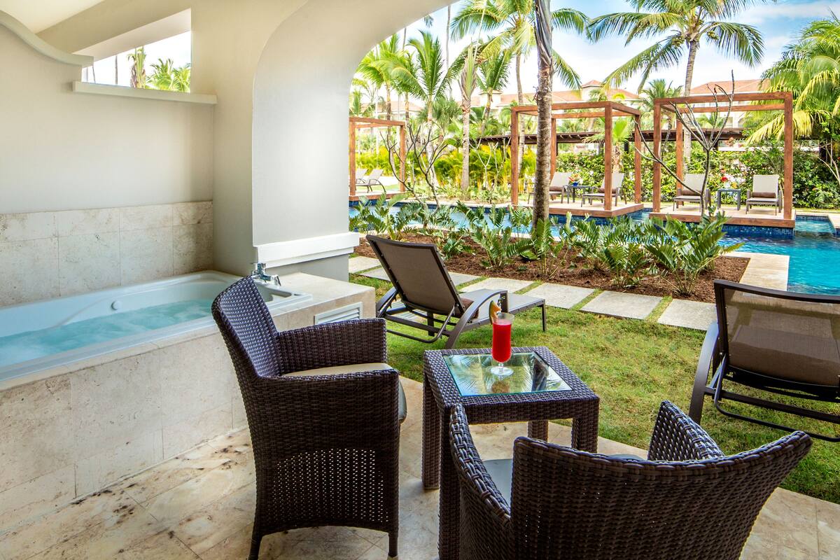 A patio area with wicker furniture, a glass table, and a view of a pool and palm trees.