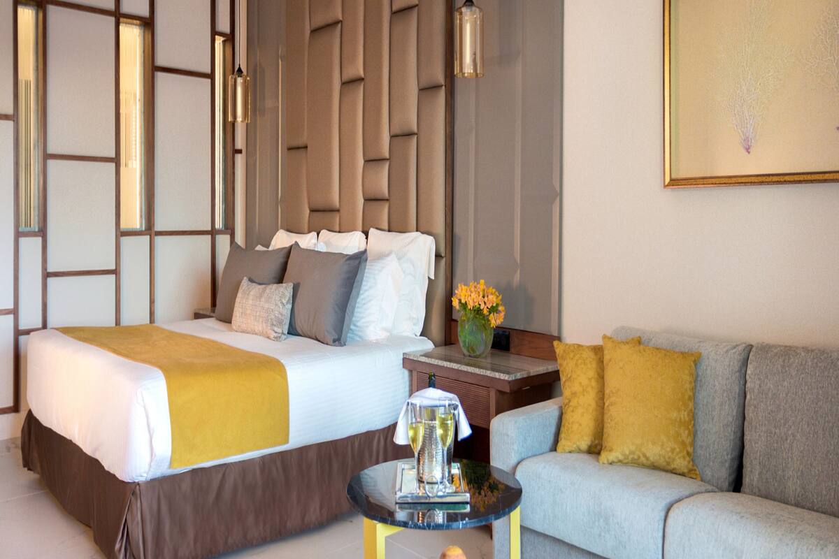A hotel room with a large bed, a sofa, a small table with fruit, and a vase of flowers.