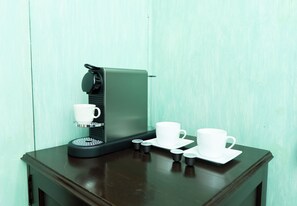A coffee machine with a cup and saucer on a wooden table against a teal wall.
