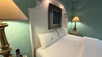 Quarto de hotel com uma cama, duas luminárias de cabeceira, um objeto decorativo na parede e um telefone na mesinha de cabeceira.