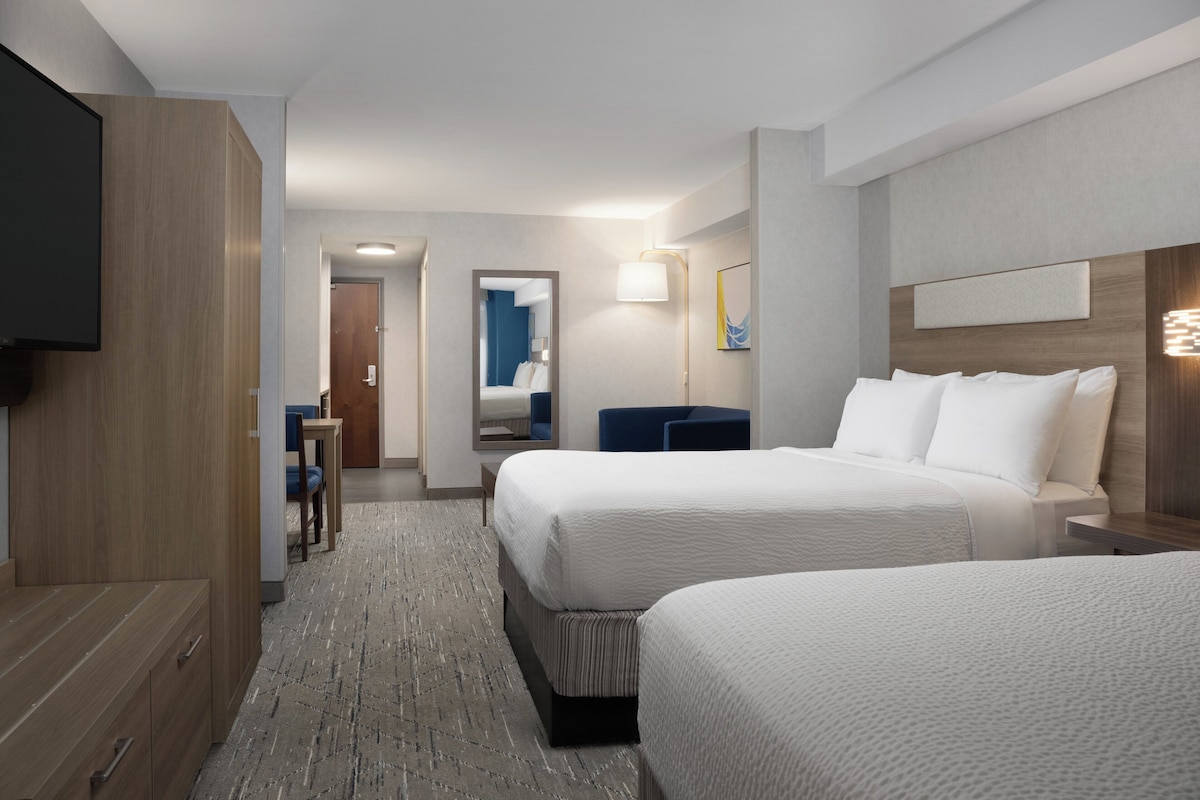 A hotel room with two beds, a TV, a desk, and a bathroom visible through an open door.