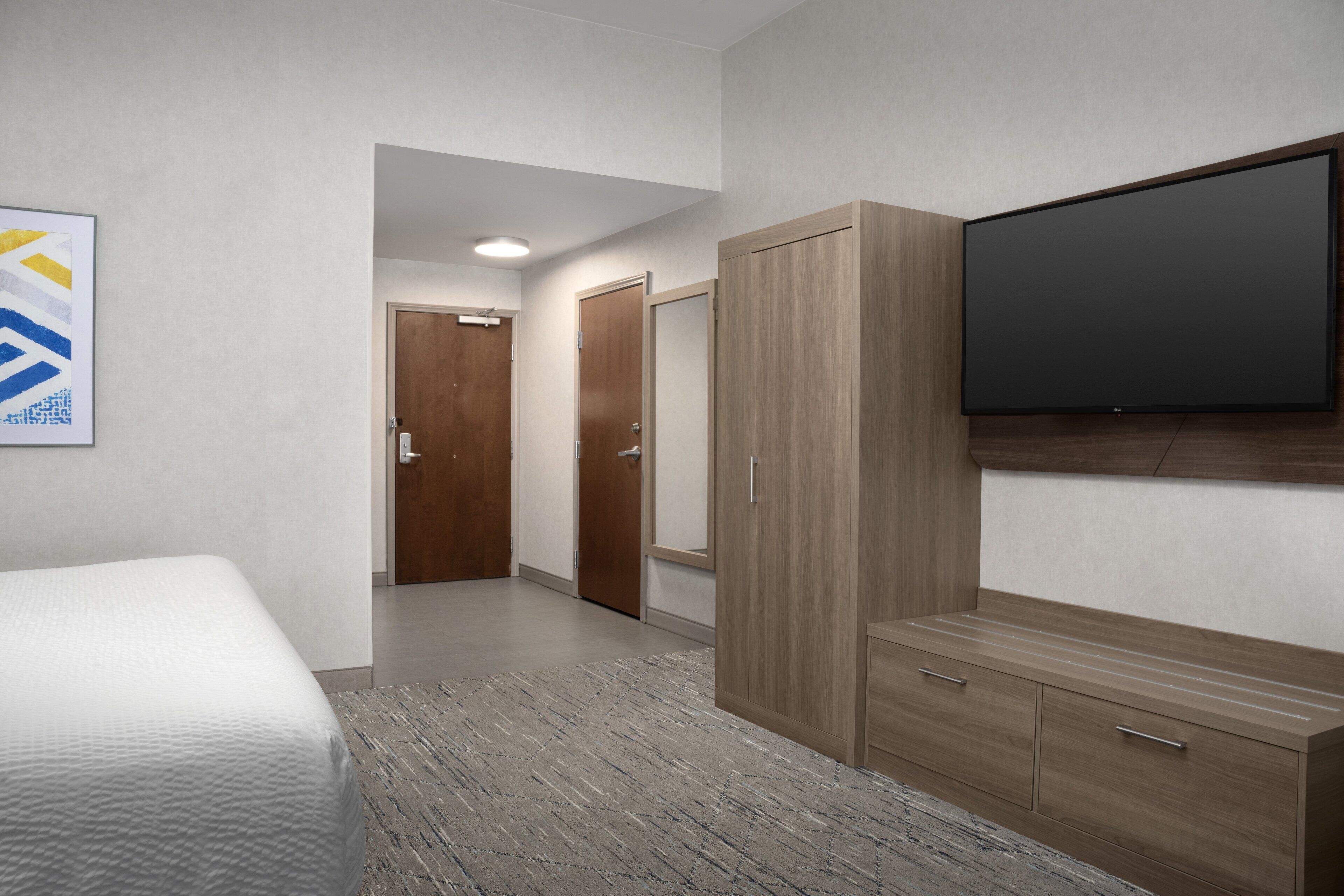Habitación de hotel con cama, armario, televisor de pantalla plana y un pasillo que conduce a otra habitación.