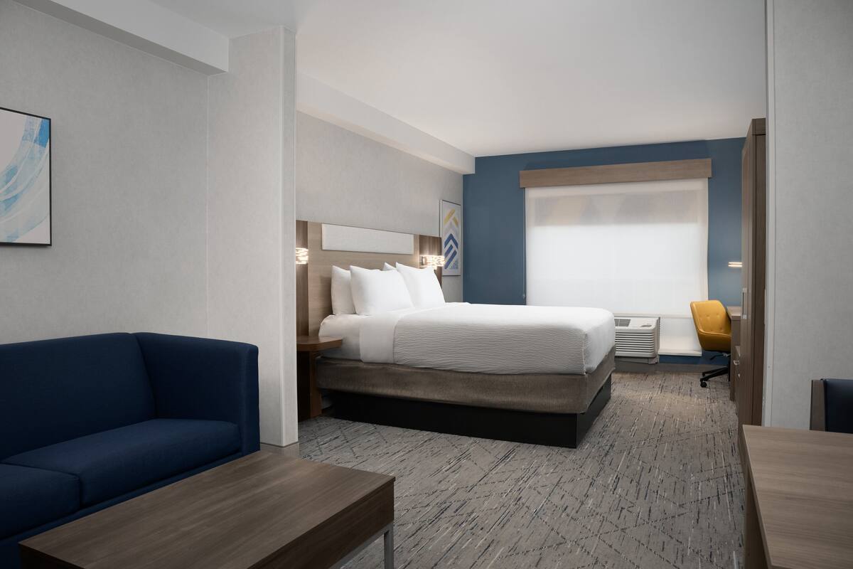 A hotel room with a bed, a blue sofa, a wooden table, and a desk.