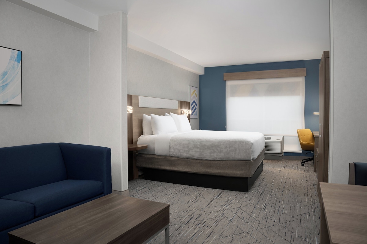 A hotel room with a bed, a blue sofa, a wooden table, and a desk.