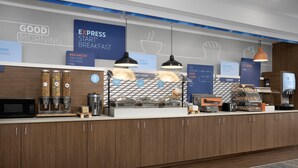 A modern breakfast area with a coffee machine, condiment dispensers, and a bakery section. - Holiday Inn Express & Suites Alexandria - Fort Belvoir by IHG (Alexandria)