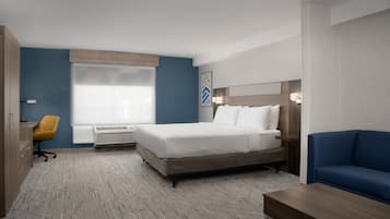 A hotel room with a bed, a desk, a chair, and a sofa.