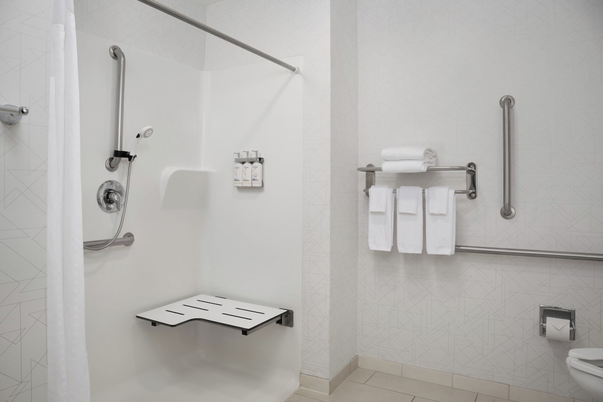 A modern bathroom with a shower, grab bars, a towel rack, and a toilet paper holder.