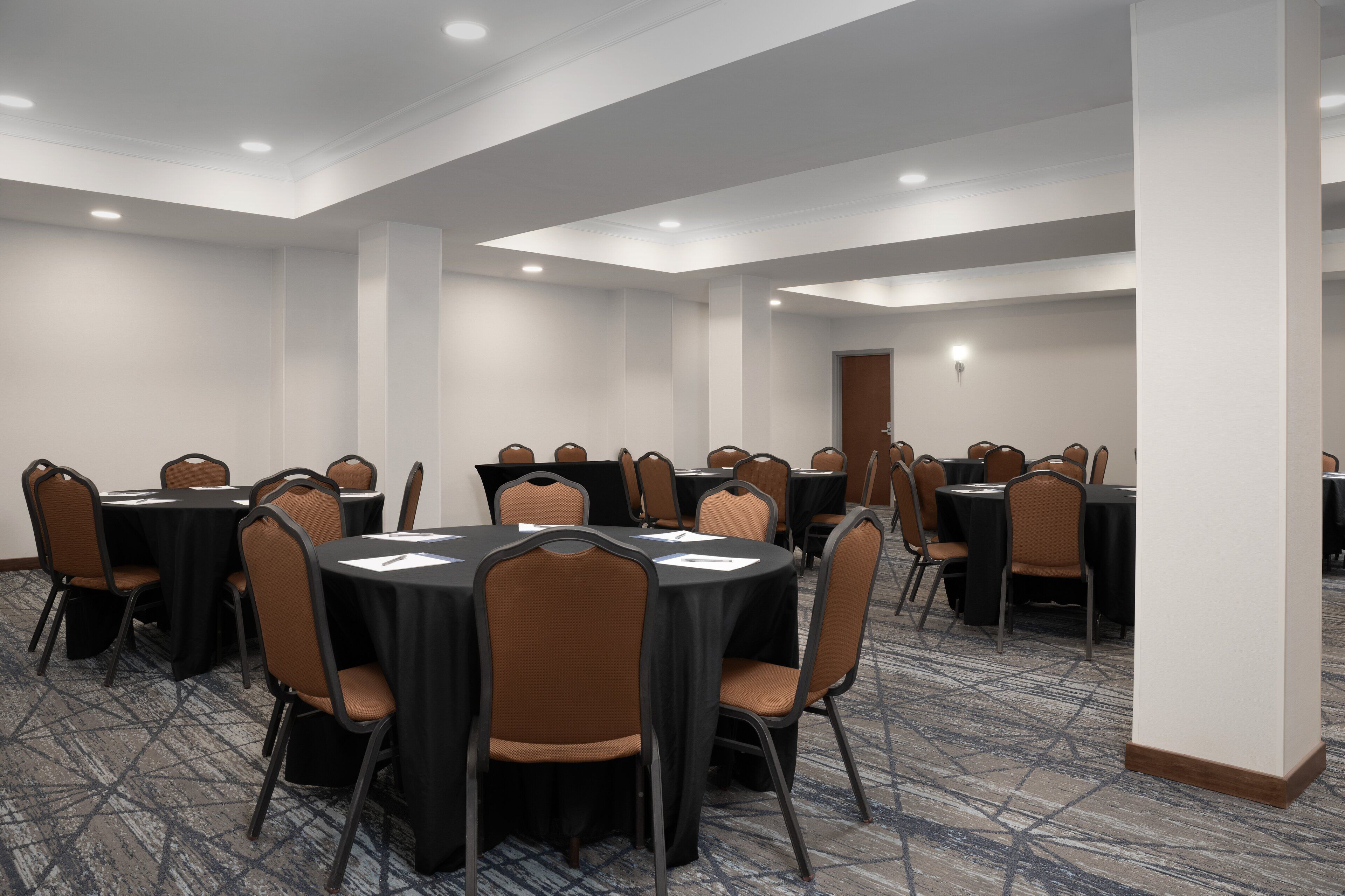 A conference room with multiple round tables and chairs, carpeted flooring, and recessed lighting.
