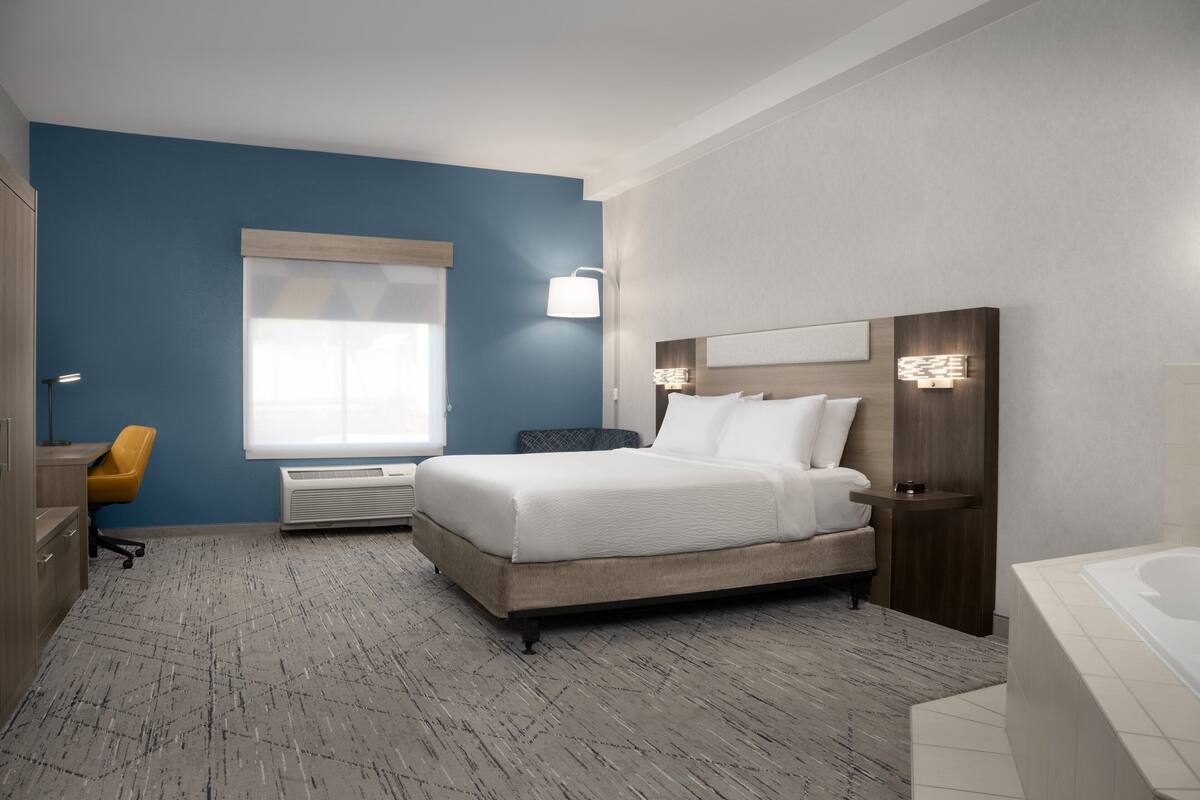 A hotel room with a bed, a desk, a chair, a window, and a bathroom.