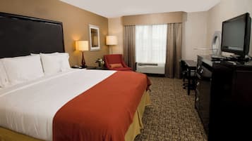 Quarto de hotel com uma cama grande, uma escrivaninha, televisão e janela com cortinas.