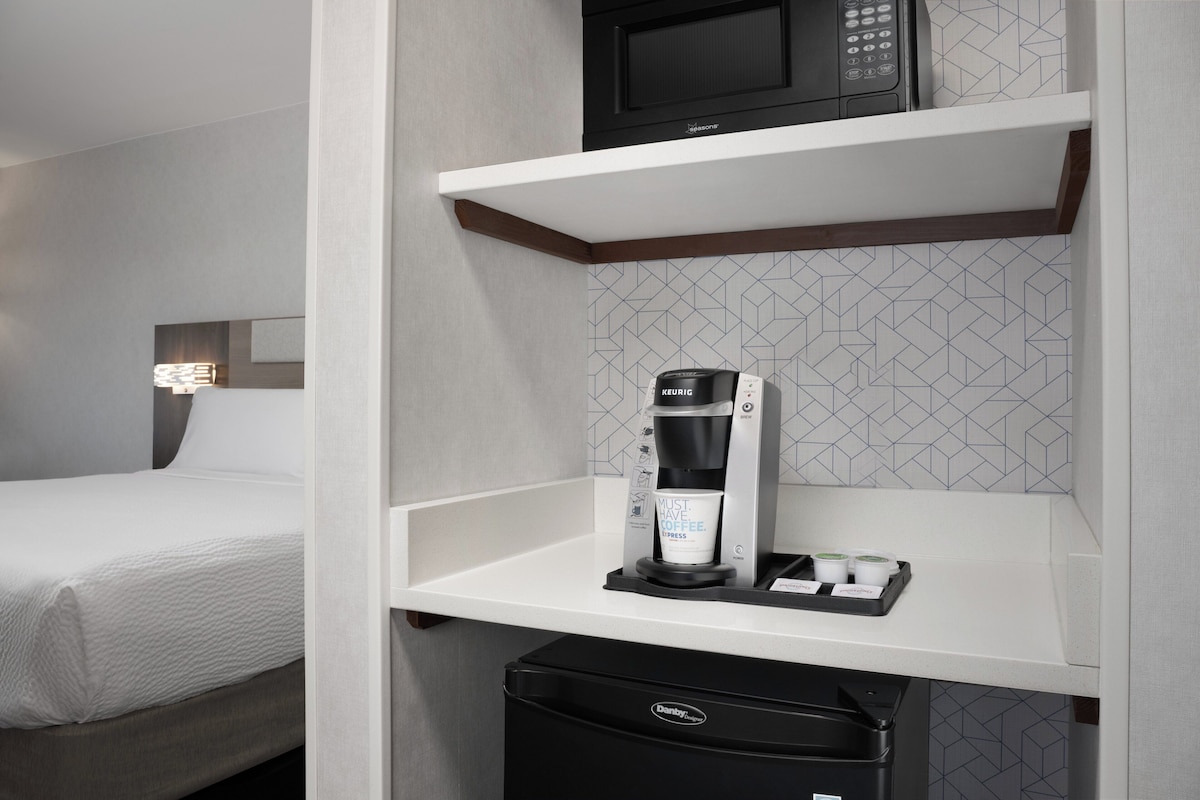 A hotel room with a bed, a coffee maker, a microwave, and a mini-fridge.