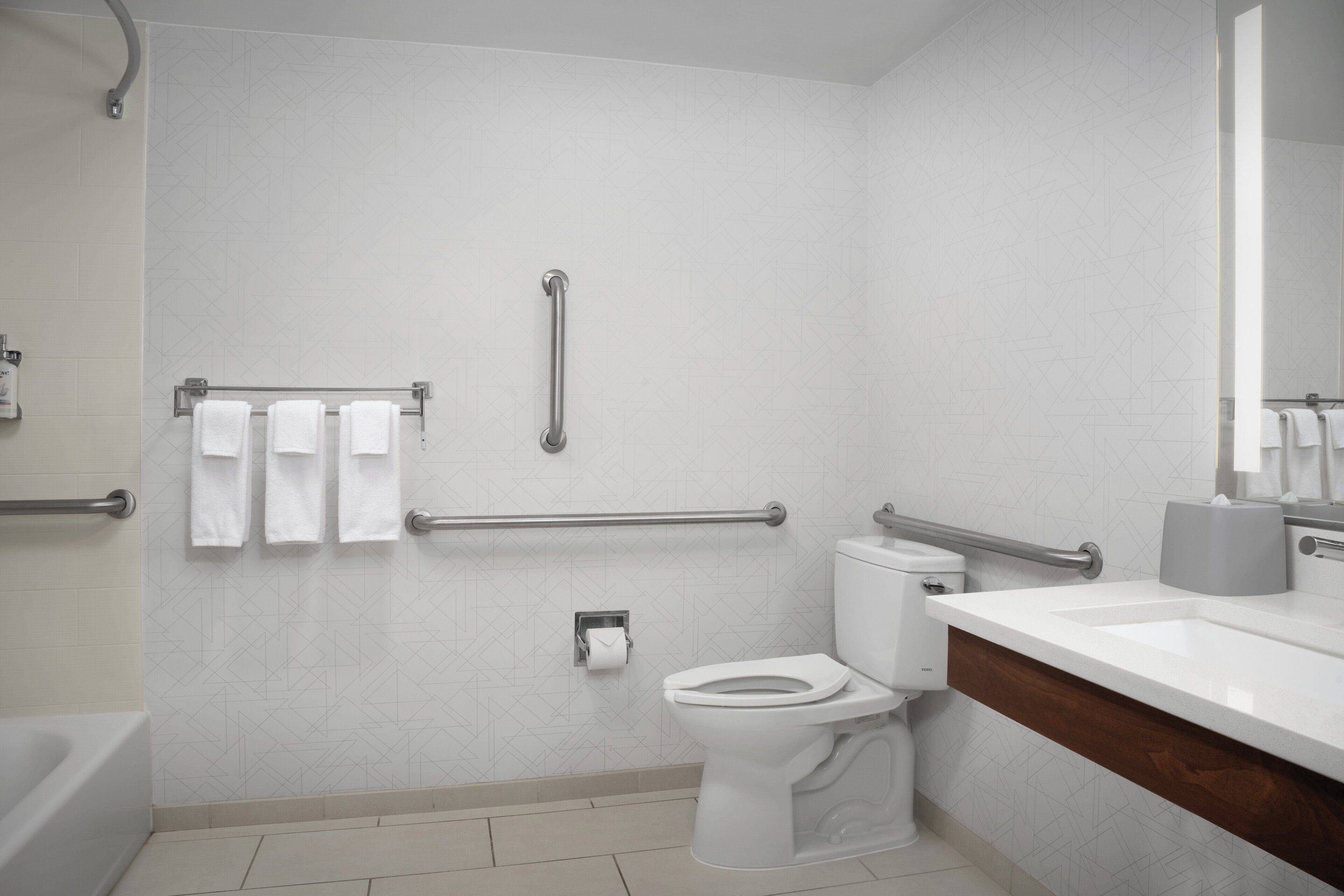 A modern bathroom with a toilet, bidet, and handrails.
