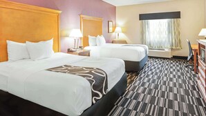 Una camera d'albergo con due letti, una scrivania, una sedia e una finestra con tende.