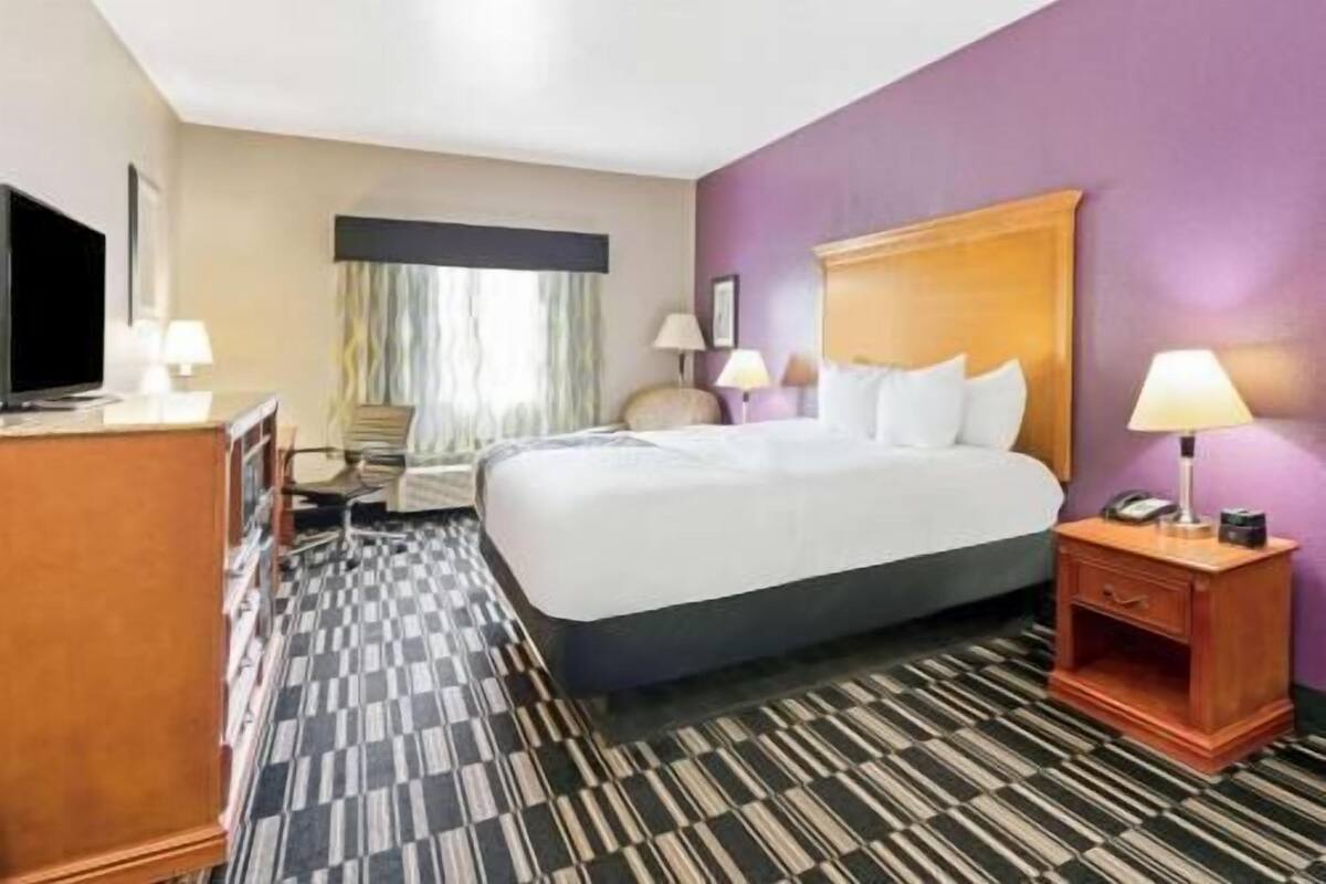 A hotel room with a bed, bedside tables, a desk, a television, and a window with curtains.